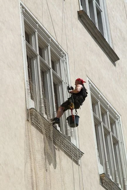 Vue de côté d’une jeune femme concentrée, portant des gants en latex, debout et nettoyant un miroir dans une pièce claire en journée